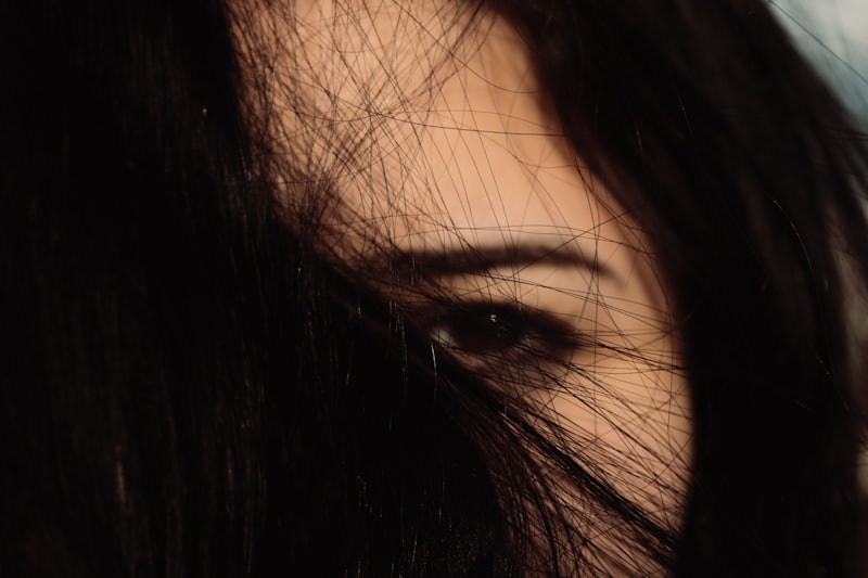 Dark editorial close-up of a defined eyebrow seen through strands of hair